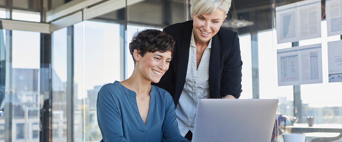 two smiling businesswomen sharing laptop