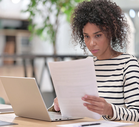 women reads paper in front of laptop