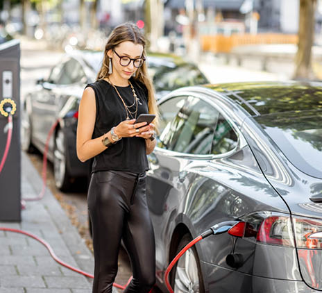 Een vrouw die op haar mobiel aan het wachten is op het laden van haar elektrische auto. 