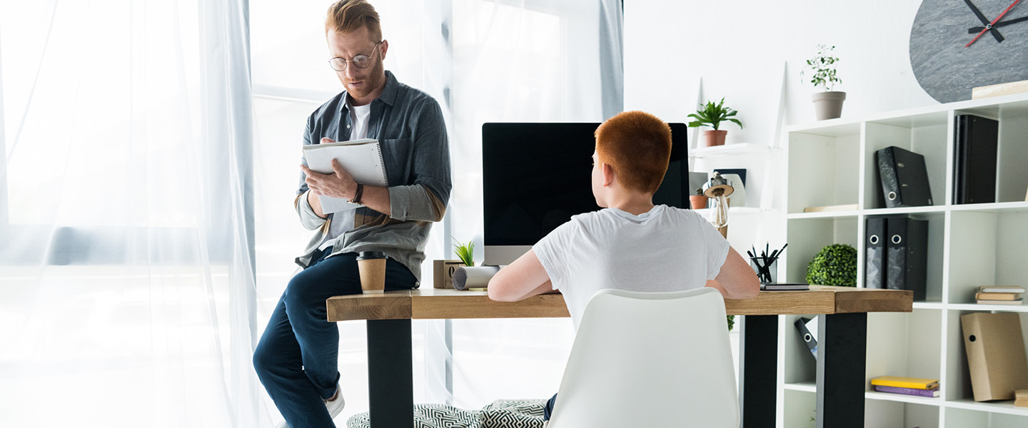 father writing to notebook son using computer