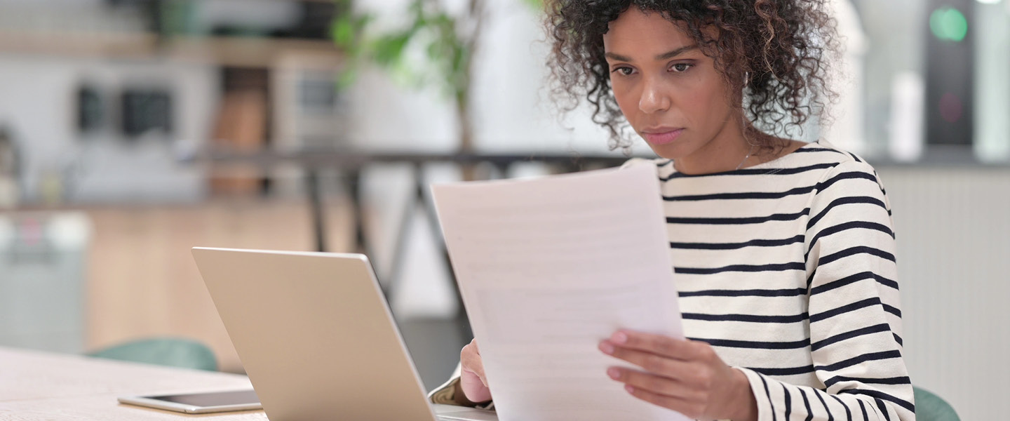 women reads paper in front of laptop